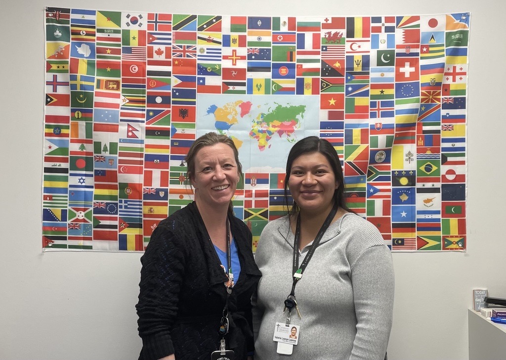 Two women smiling at the camera with an international flag collage behind them