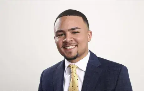 Male sutdent wearing a navy blue jacket, white shirt and tie, medium shot