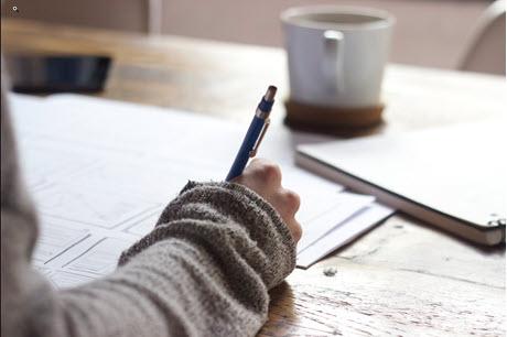 Person writing in notebook with a mug in front of them