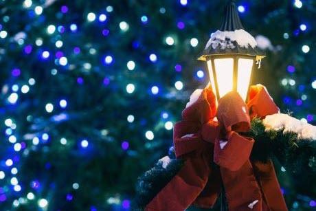 Lighted lamp post with red bow on it with multi-colored lights in background