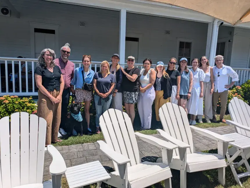 Group of people posing in front of a porch with white Adirondack chairs in the foreground